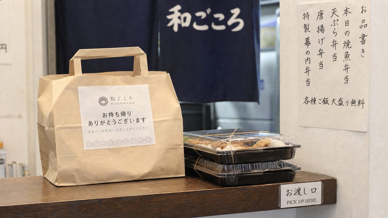 飲食店の受け取りカウンターに置かれた持ち帰り用の紙袋と弁当容器