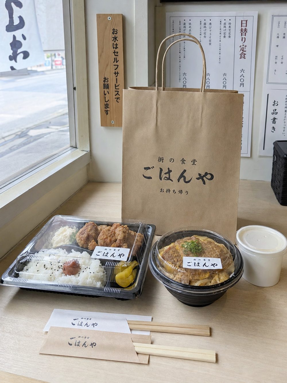 小さな飲食店のカウンターに並んだ持ち帰り用の紙袋とテイクアウト容器